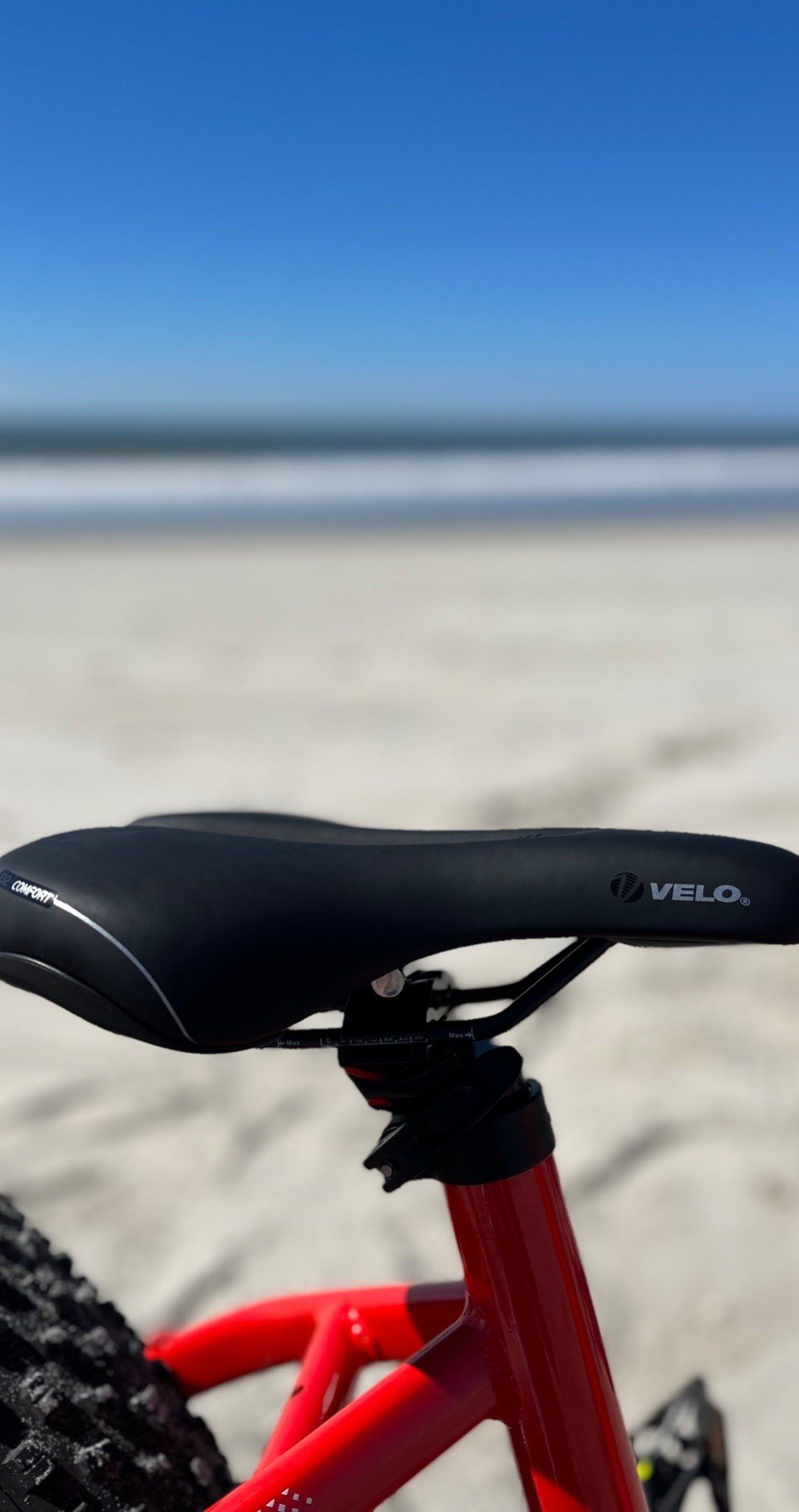 Close-up of a padded black saddle on a red e-bike frame against a blue sky