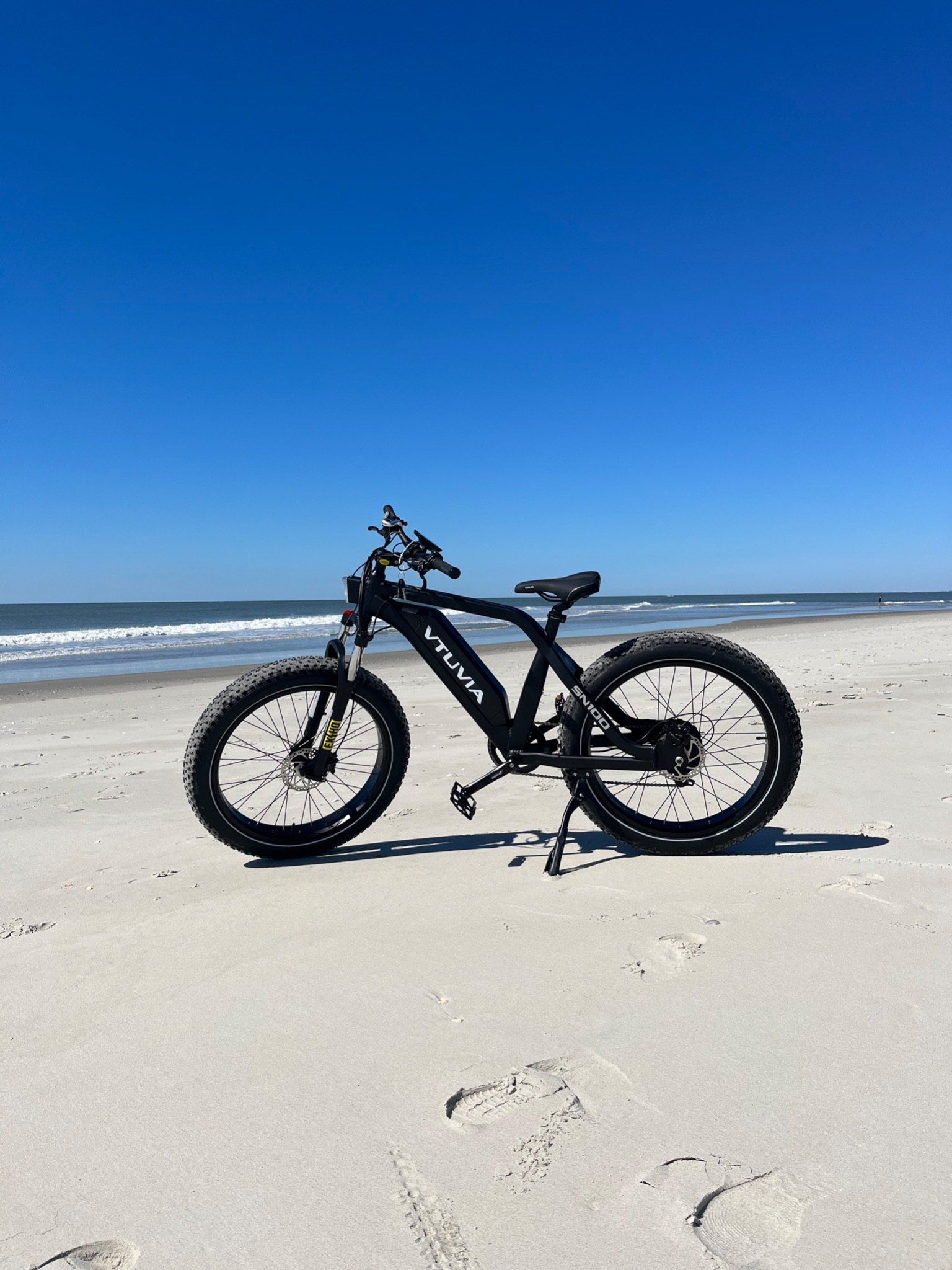Black fat-tire step-through e-bike standing on the sand in front of the ocean