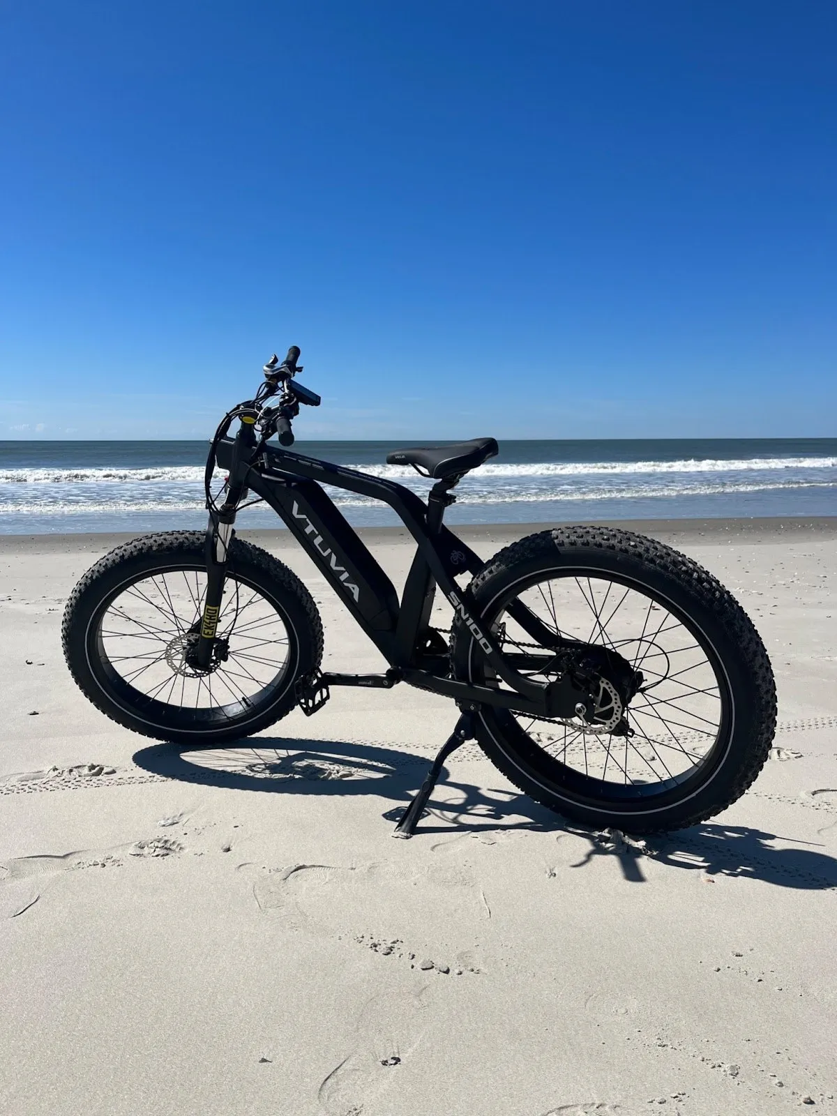 Black fat-tire e-bike on its kickstand on smooth sand, blue sky above