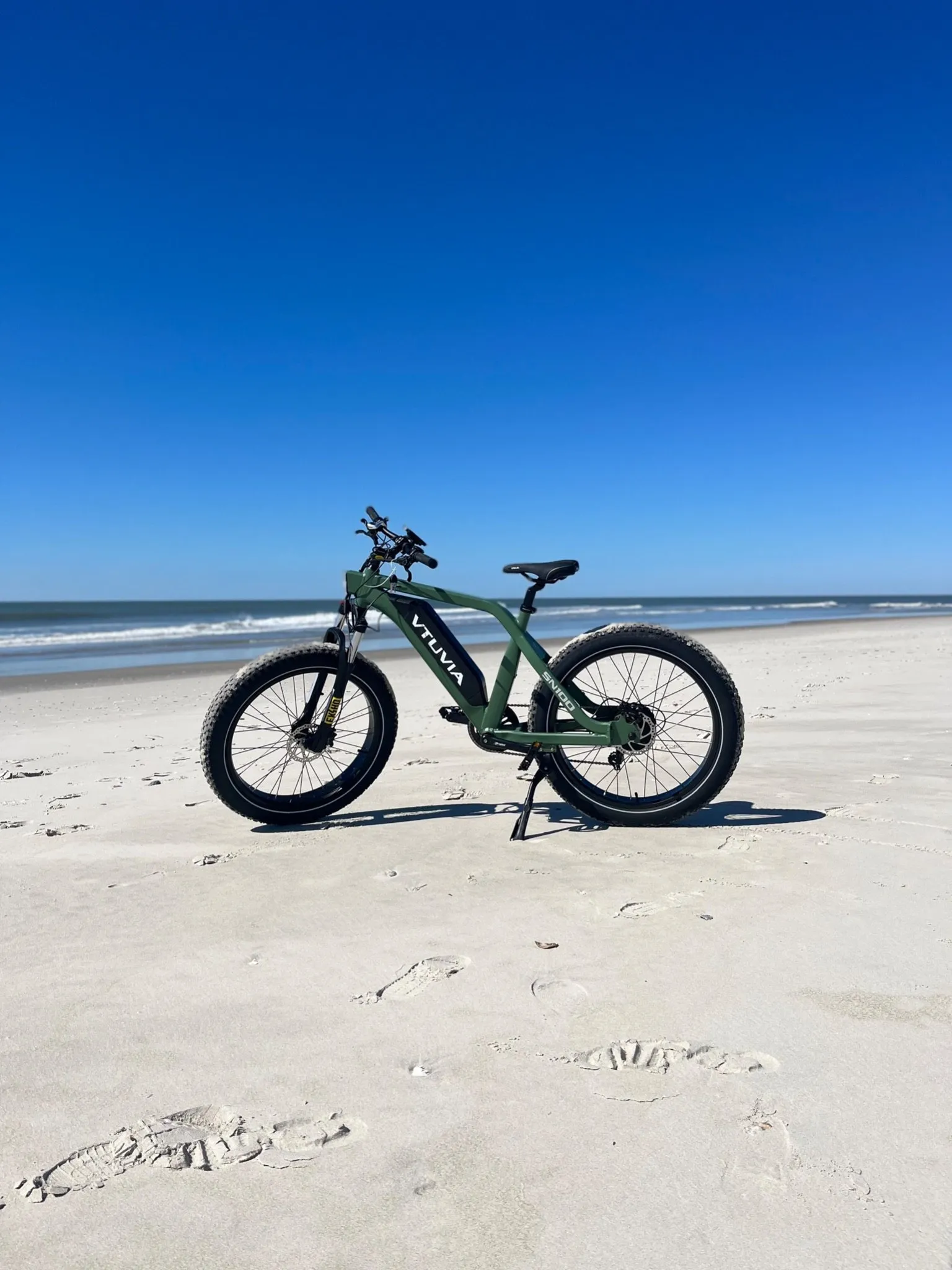 Green fat-tire step-through e-bike standing on the sand in front of the ocean